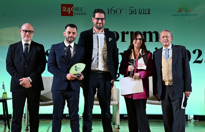 5 persone in piedi, con vestiti eleganti, posano sorridendo su sfondo che mostra il logoe de Il Sole 24 Ore. la seconda persona da sinistra tiene n mano un premio, la quarta, una donna, dei foglie e un microfono.