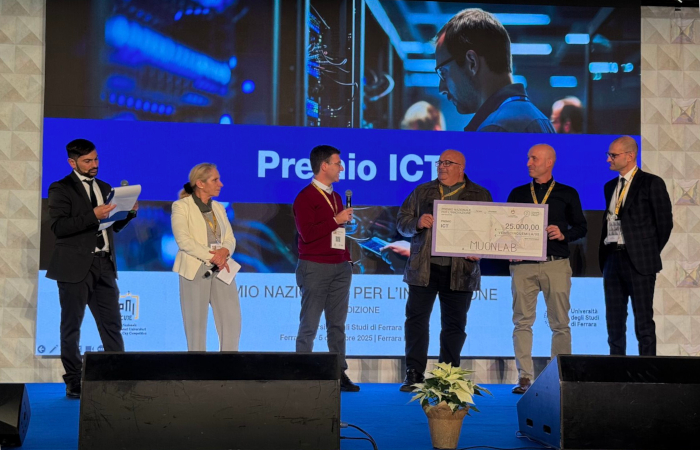 6 persone su un palco, le tre sulla destra tengono in mano un grossa targa con scritto MuonLab, 25000€. sullo sfondo uno maxischermo con la scritta Premio ICT