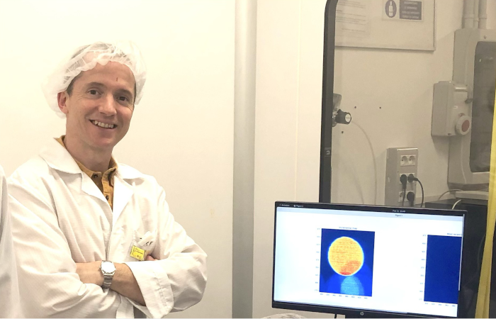 sulla sinistra figura a mezzobusto sorridente con le braccia conserte che indossa camice e cuffia. a destra schermo di computer che mostra immagine in falsi colori di un wafer in silicio